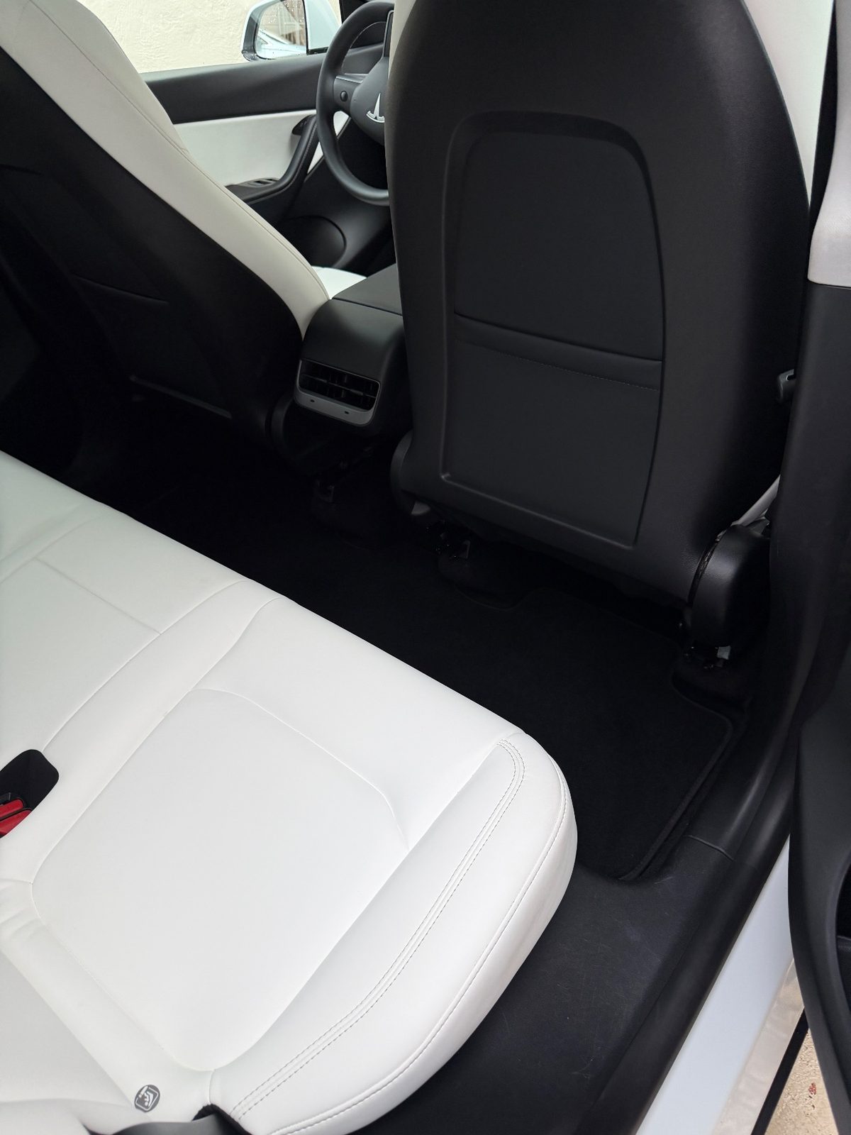 Rear footwell of a white Tesla Model Y after detailing, with a clean carpet mat