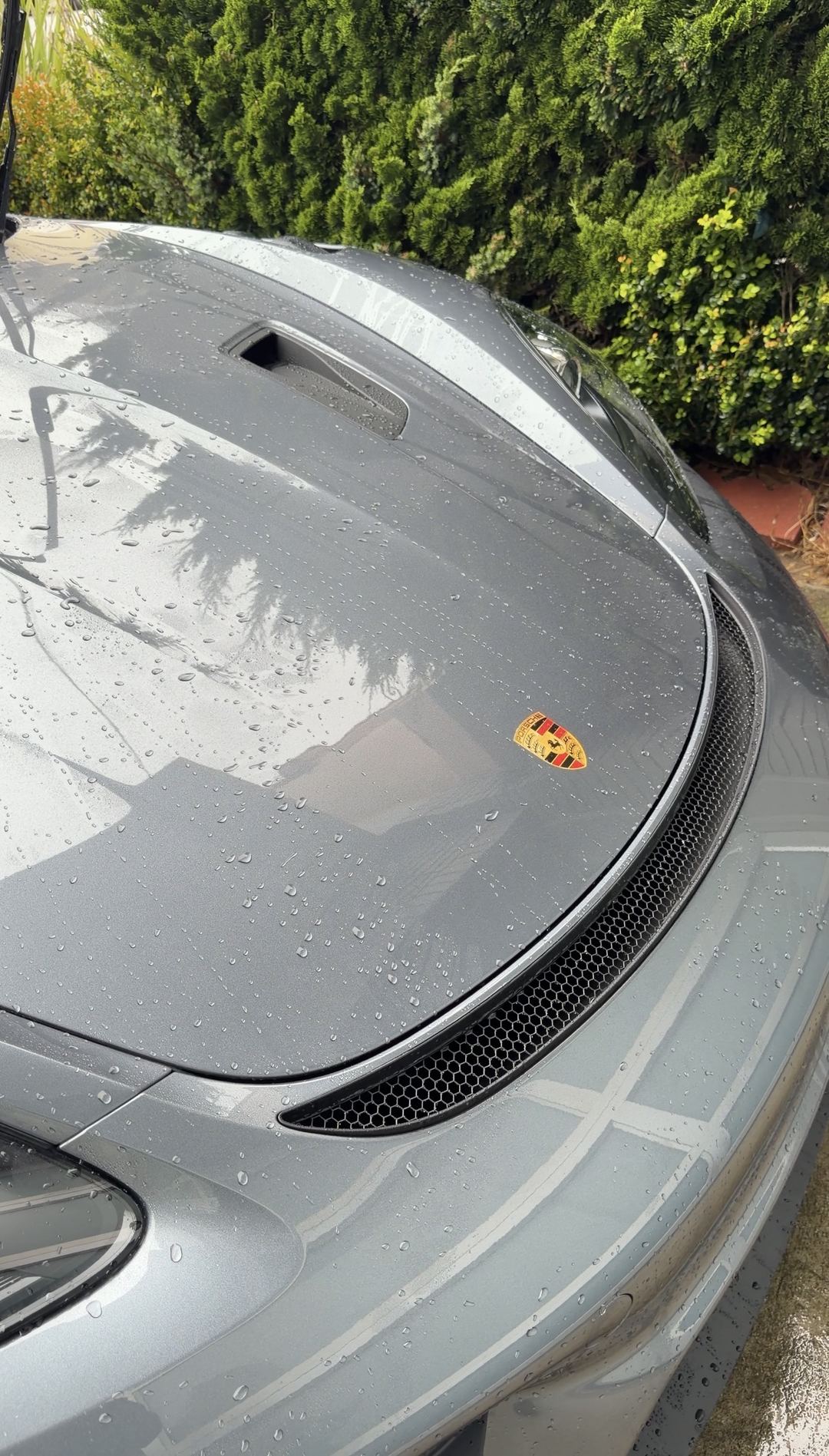 The bonnet of a grey Porsche 718 Spyder RS under rinse water after the bird dropping was washed off.