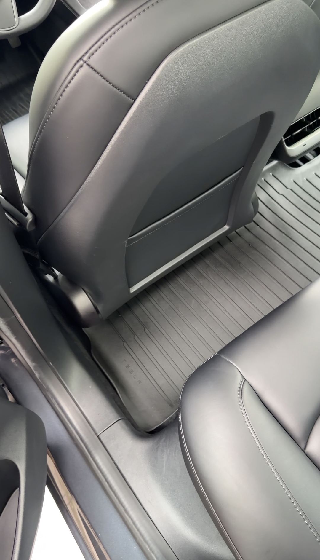 Rear footwell behind the driver seat of a Tesla Model 3 after cleaning, clean TESLA floor mat