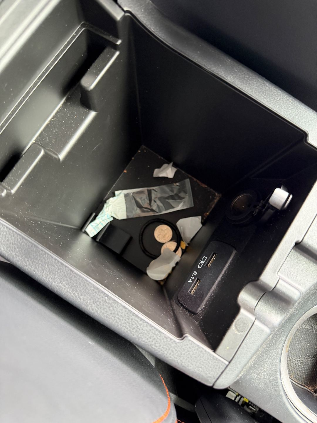 Centre armrest storage bin of a Subaru Crosstrek before detailing, holding tissues, wrappers and coins