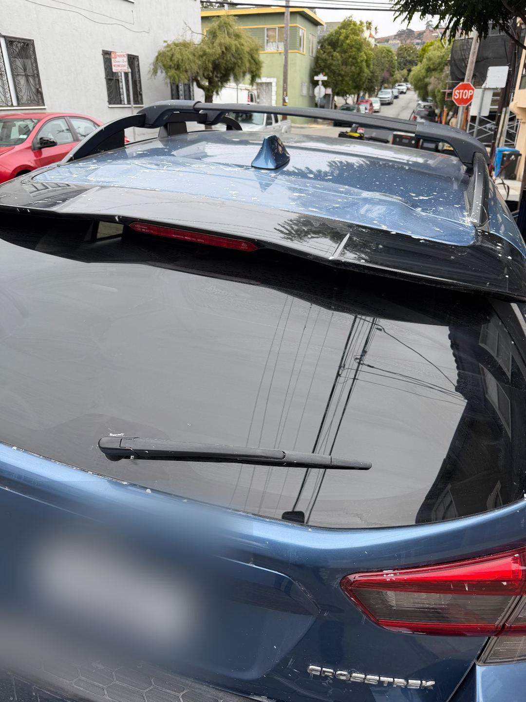 Rear hatch and roof spoiler of a blue Subaru Crosstrek before washing, spattered with white spots