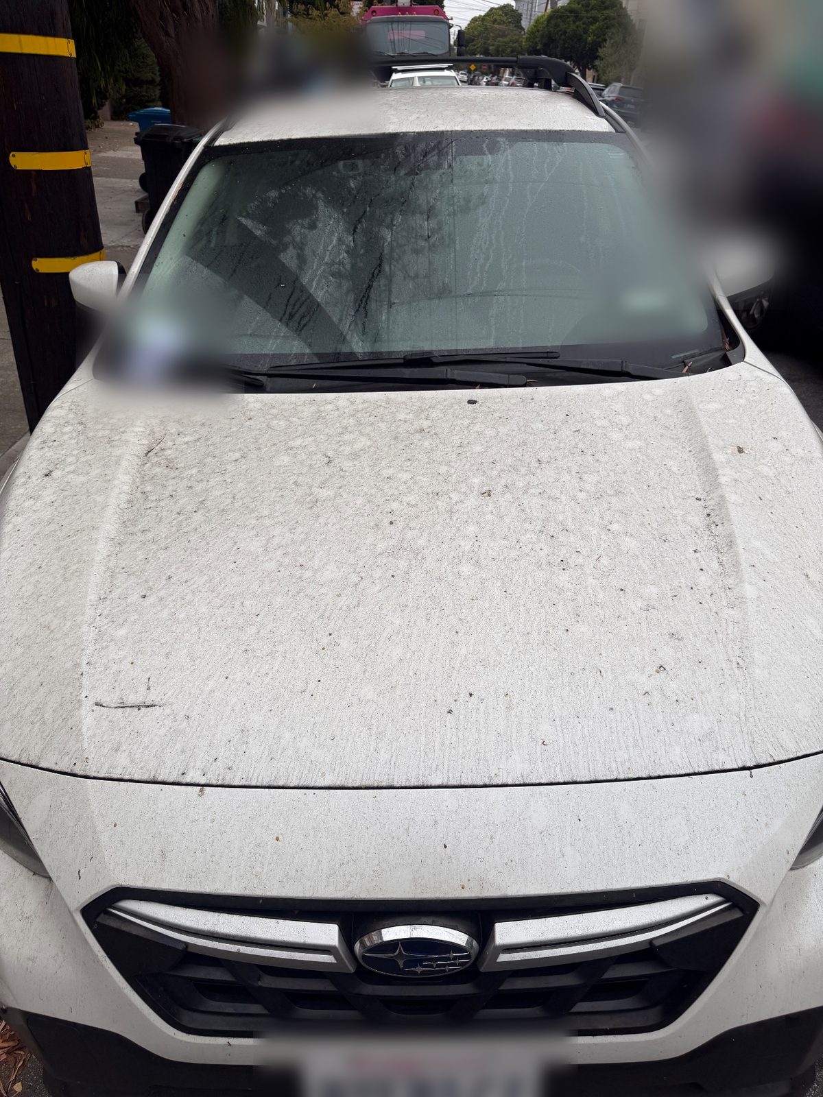 Front of a white Subaru Crosstrek before washing, hood and windshield covered in dust and water spots