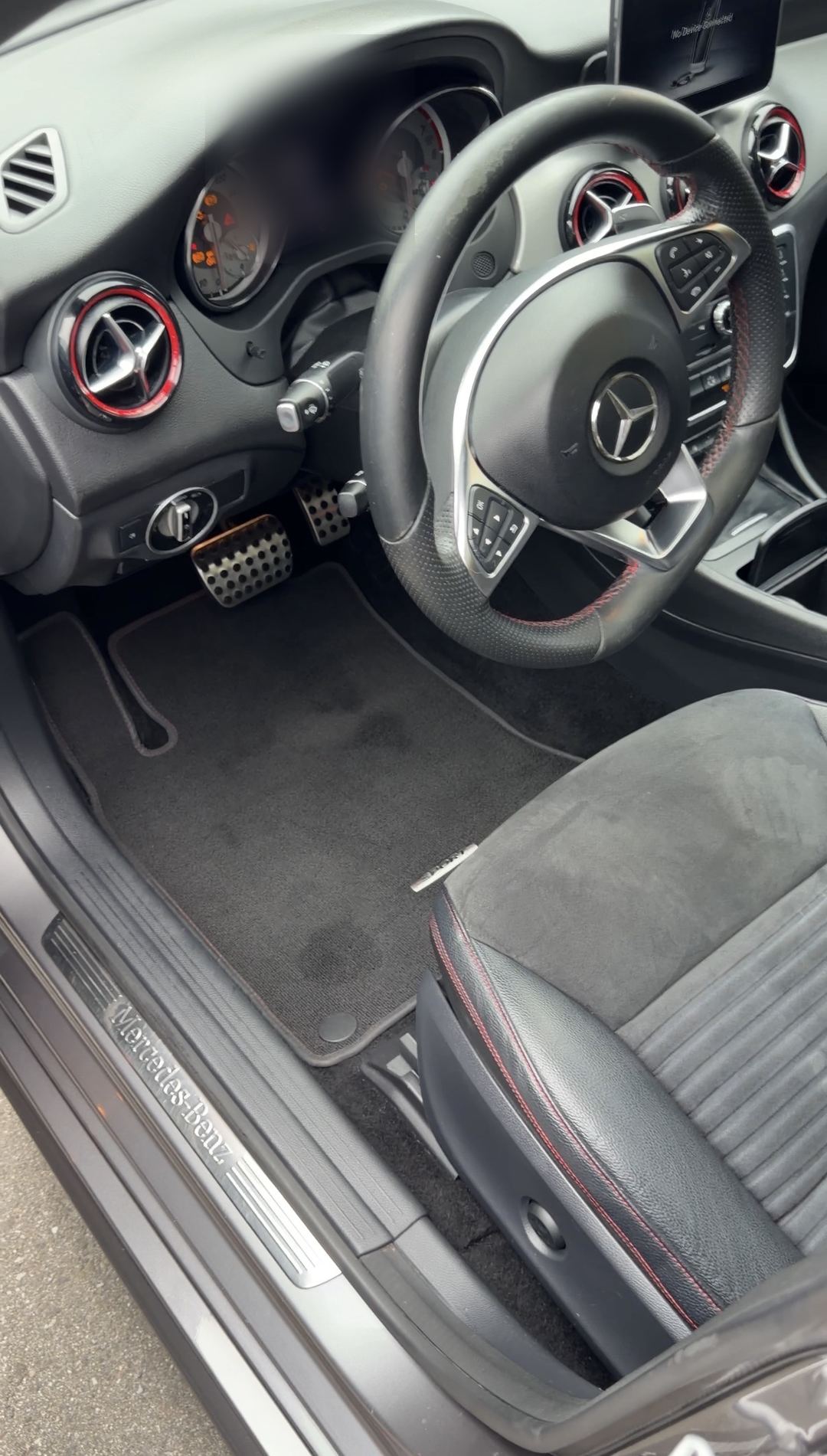 Cleaned driver's cockpit of a Mercedes-Benz CLA250 with sport steering wheel, aluminium pedals and illuminated sill plate