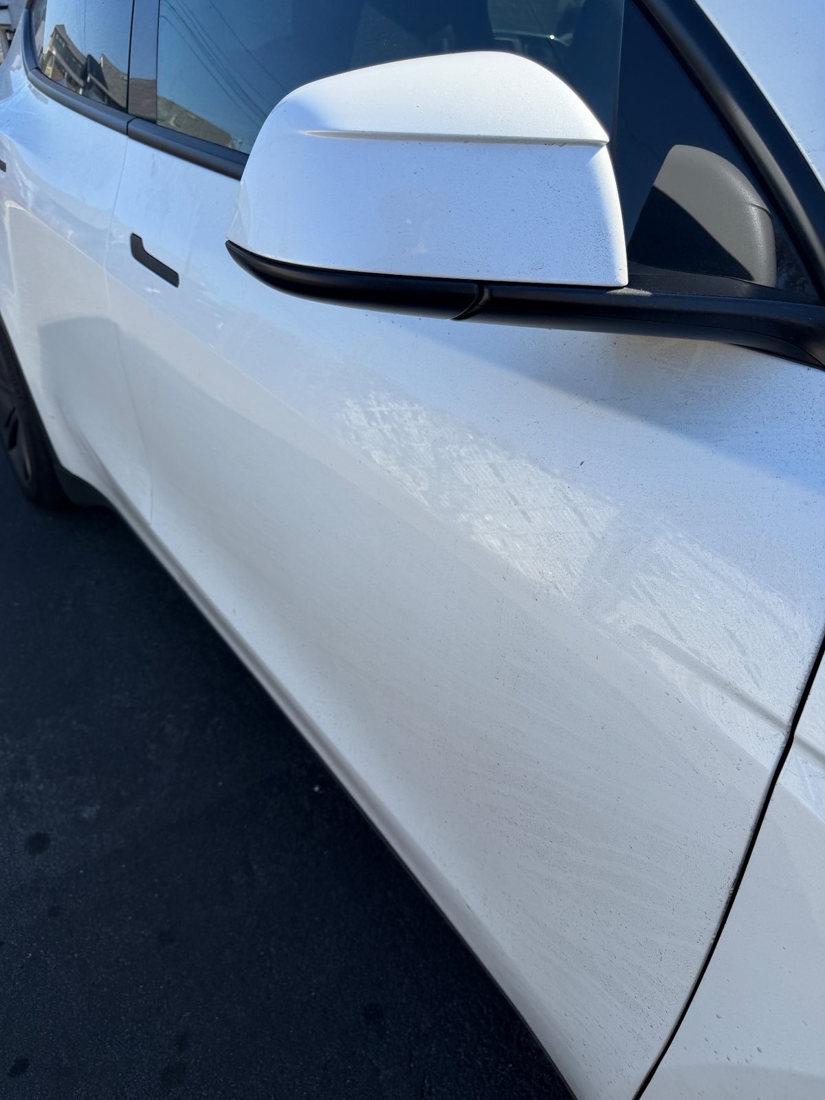 Front door and mirror of a white Tesla Model Y before washing, dust film and dried water streaks