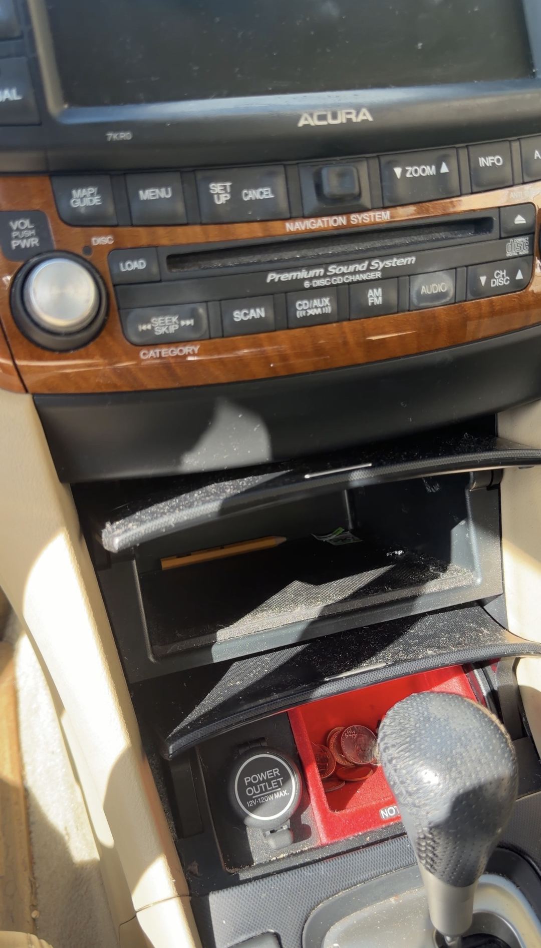 Centre console and audio stack of an Acura sedan before detailing, with dust on the wood trim and loose coins in the open change tray.