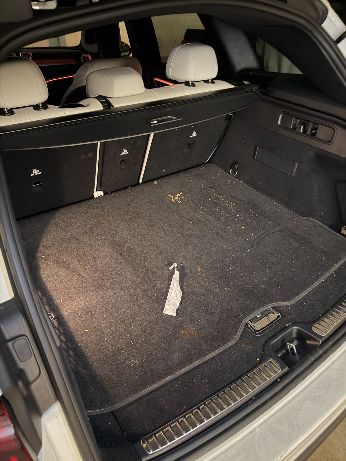 Cargo area of a white Mercedes GLC before cleaning, mat scattered with debris and a crumpled paper strip