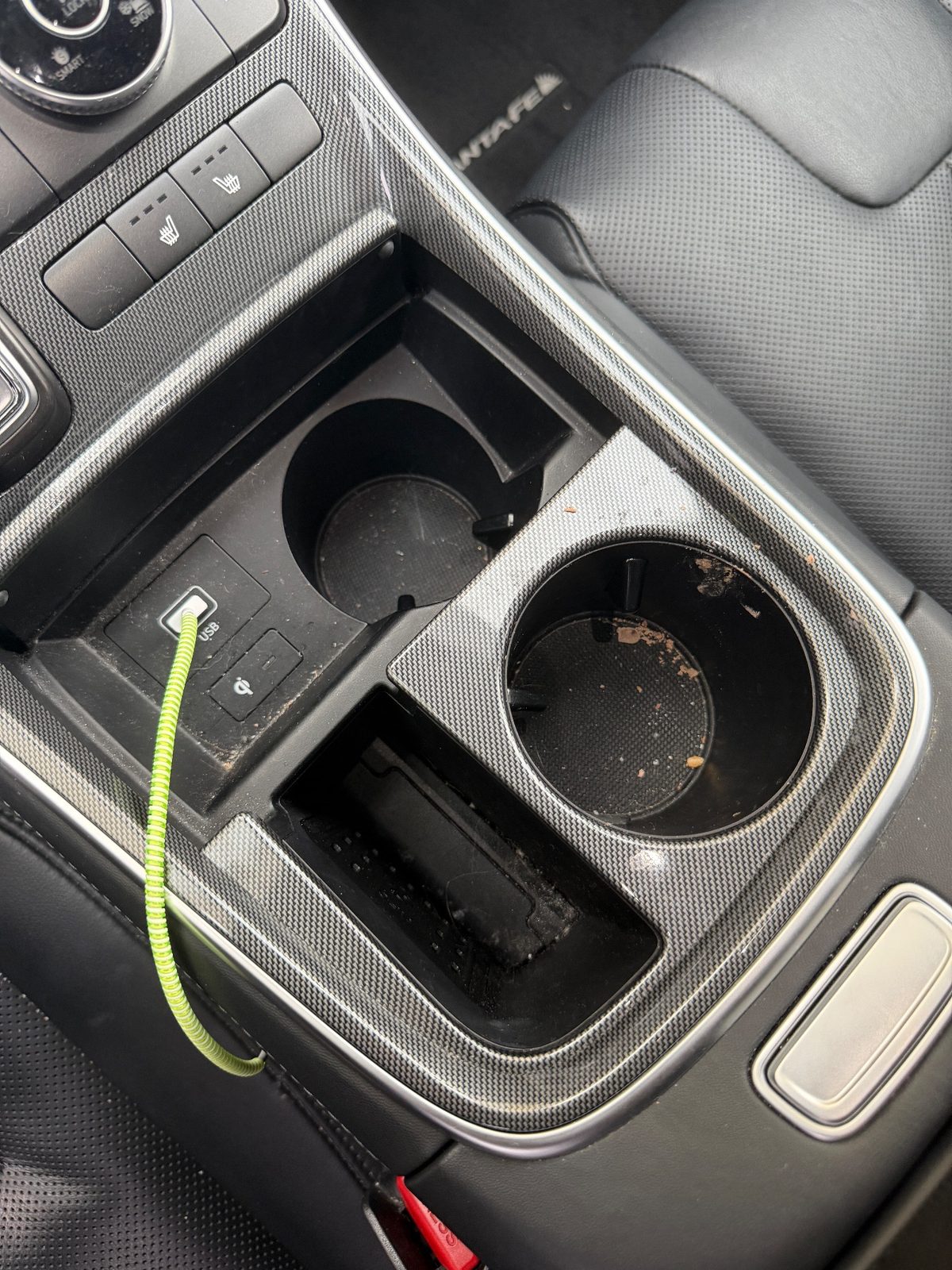 Dirty cupholders and charging tray in the centre console of a Hyundai Santa Fe before detailing