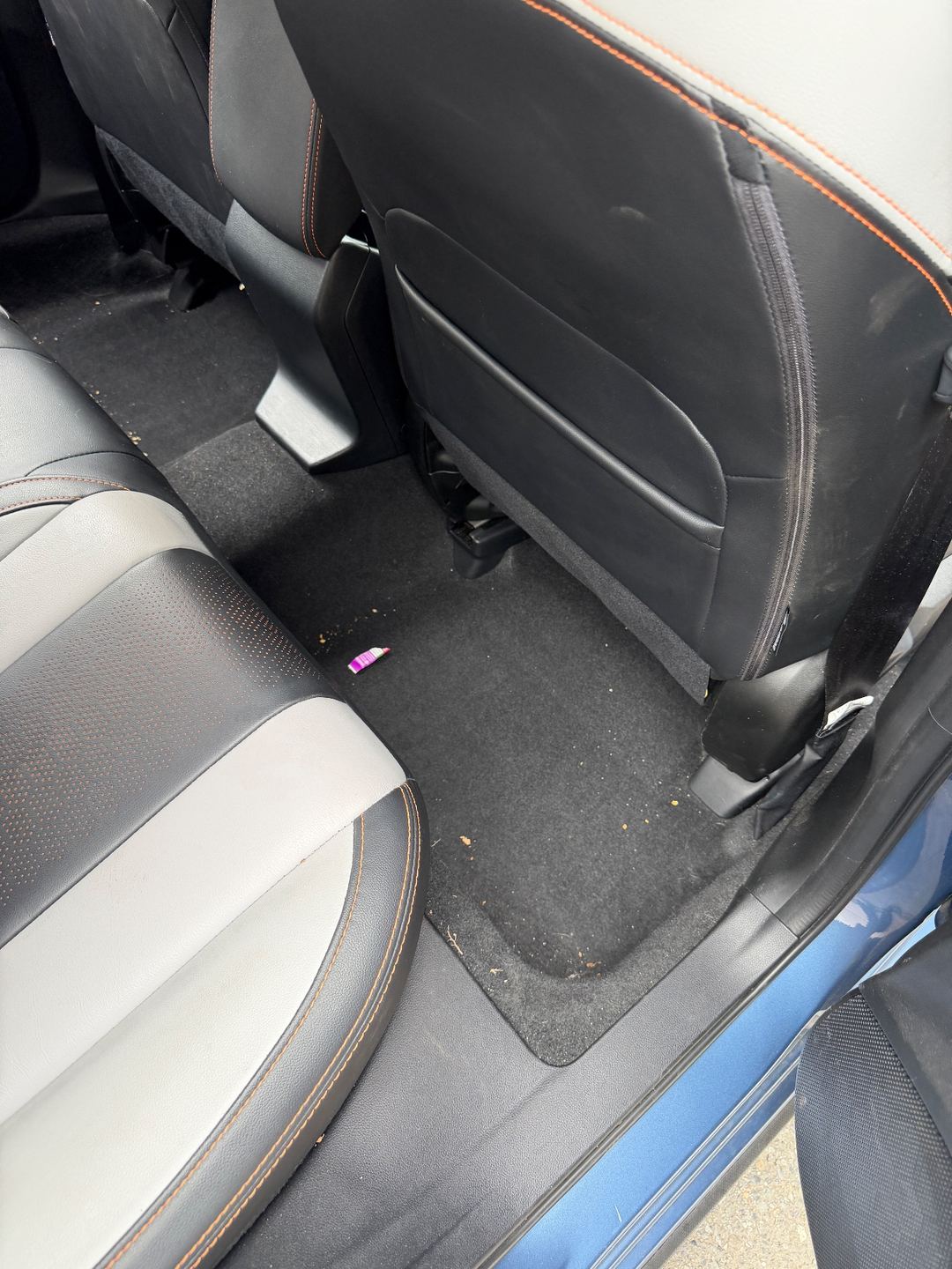 Rear passenger-side footwell of a Subaru Crosstrek before detailing, with crumbs and a wrapper on the carpet