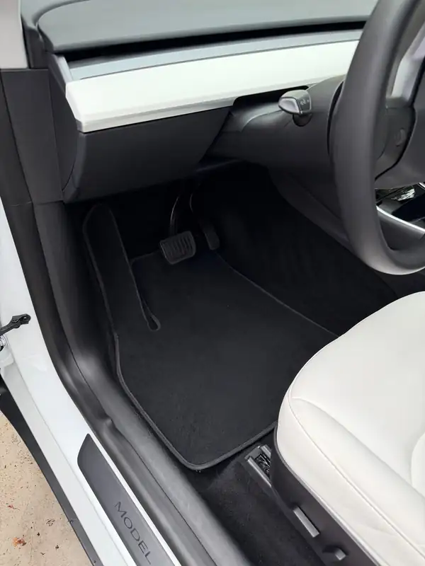 Driver footwell of a white Tesla Model Y after detailing, with a clean vacuumed carpet mat