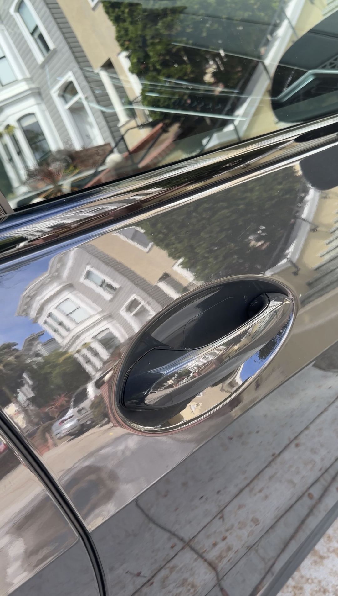 Close detail of the chrome door handle on a dark grey BMW X5, reflecting a San Francisco Victorian