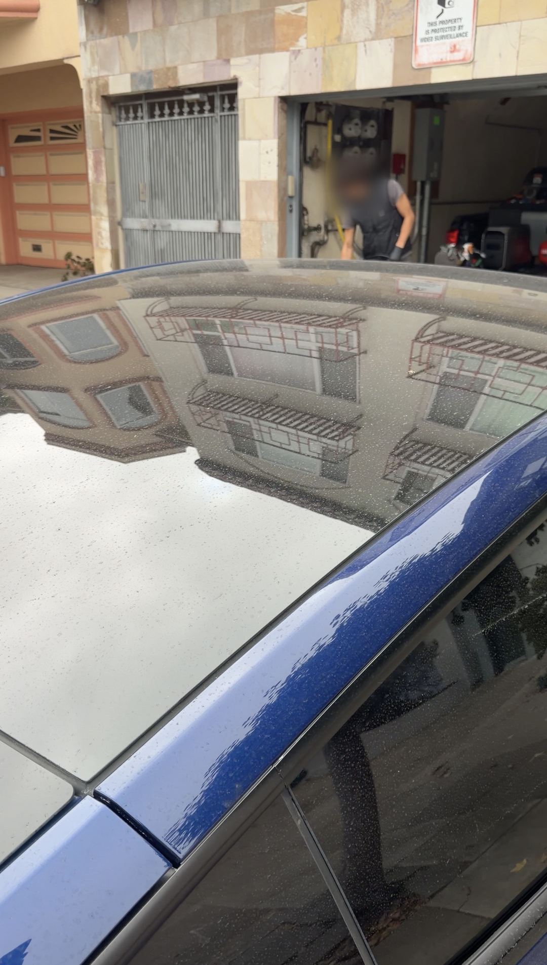 Panoramic glass roof of a blue Tesla Model Y covered in dried water spots before washing.