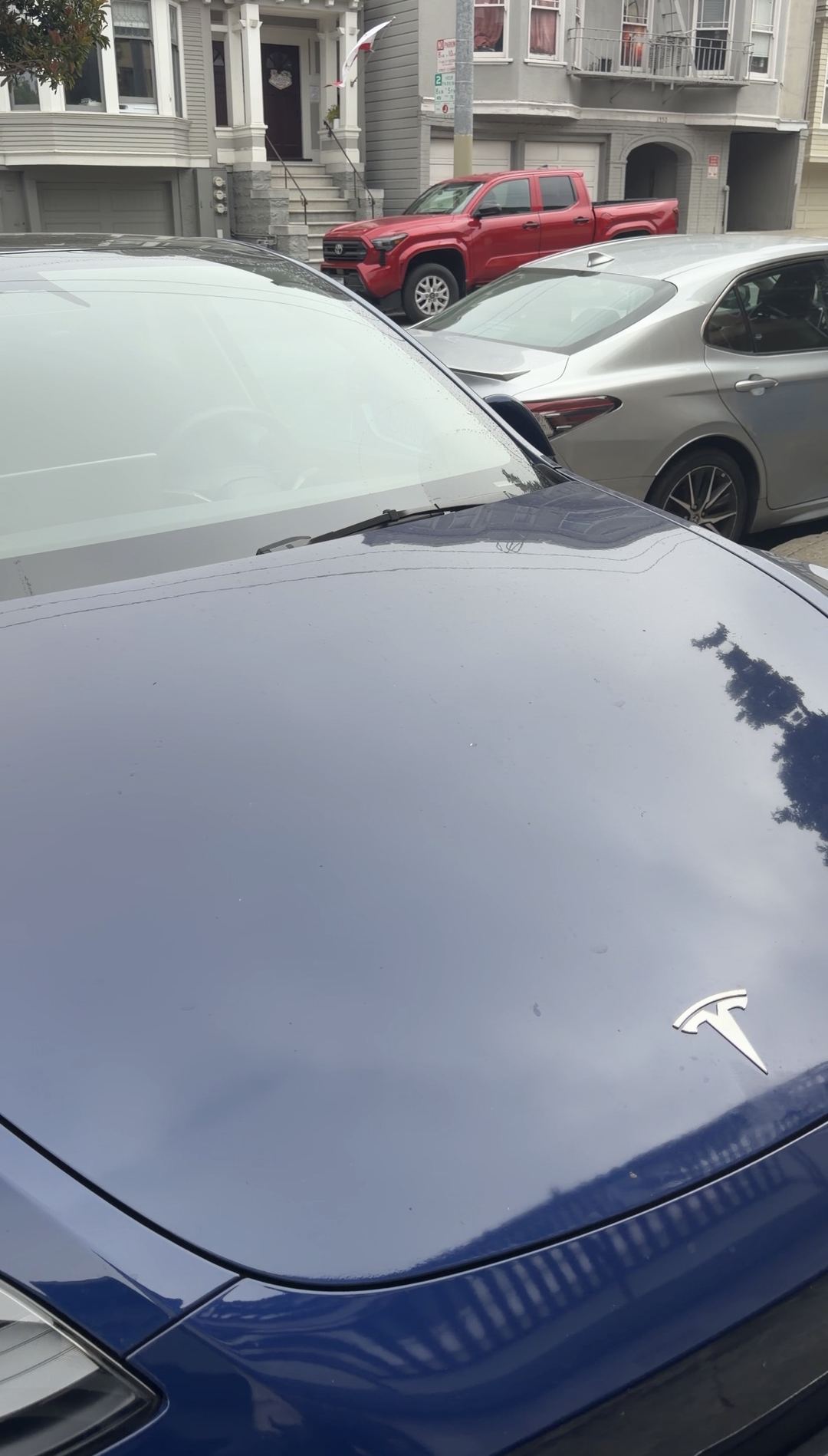 Dusty, water-spotted bonnet and windscreen of a blue Tesla Model Y before washing.