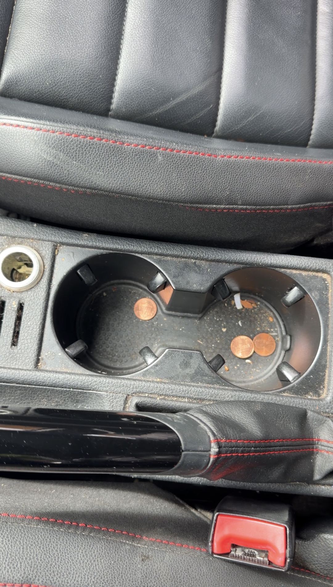 Front cupholders of a VW GTI with loose pennies and crumbs before cleaning