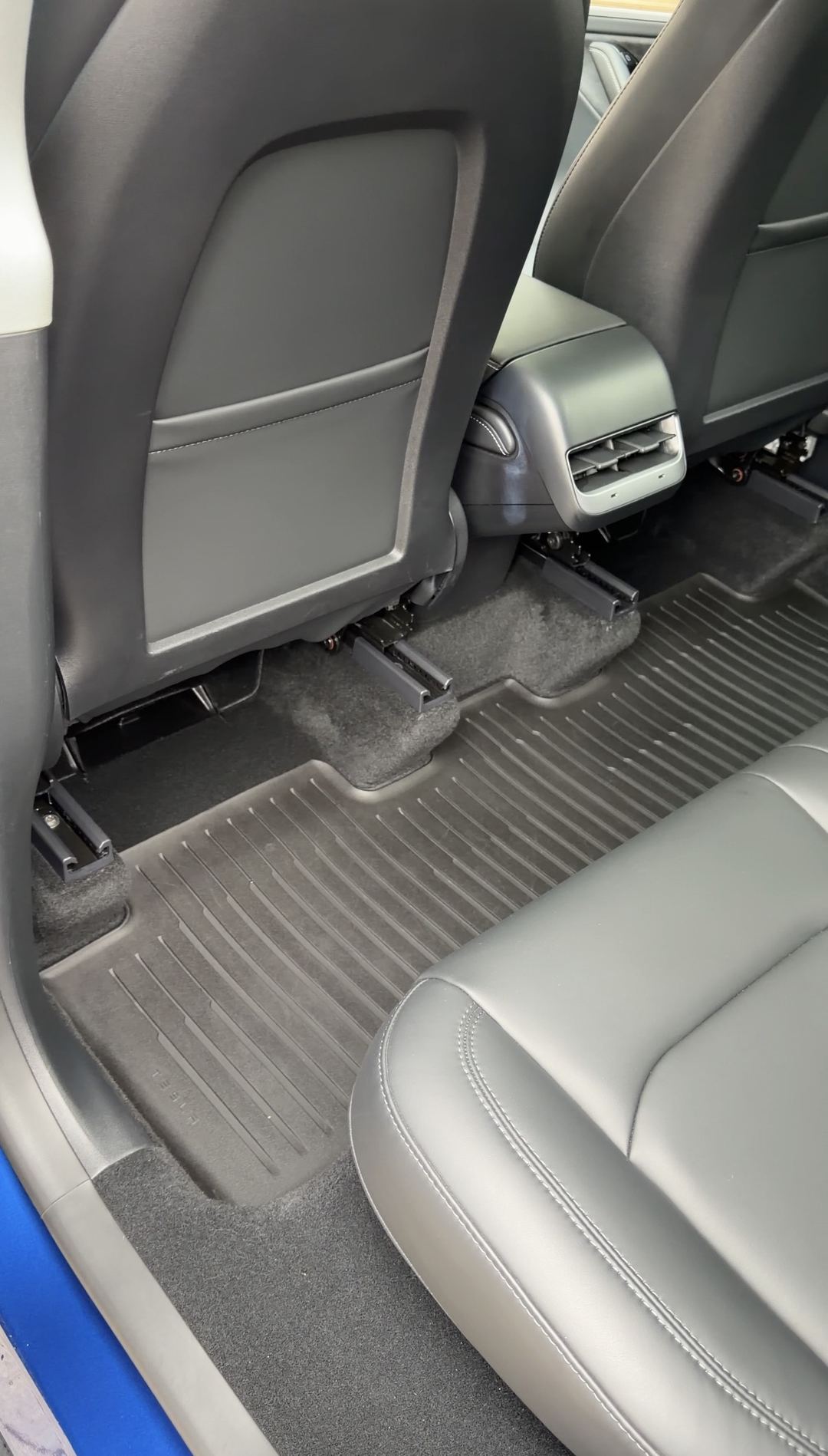 Clean rear driver-side footwell of a Tesla Model Y with the Tesla floor liner refitted after detailing.
