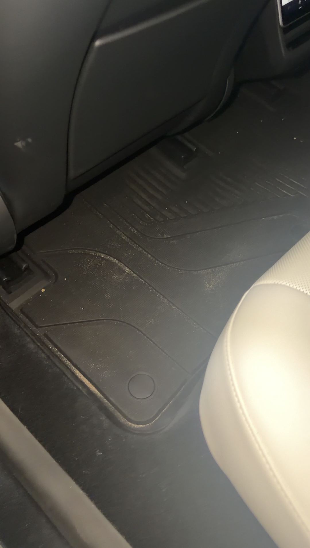 Rear driver-side footwell of a Tesla Model 3 before detailing, the black all-weather mat covered in sandy grit
