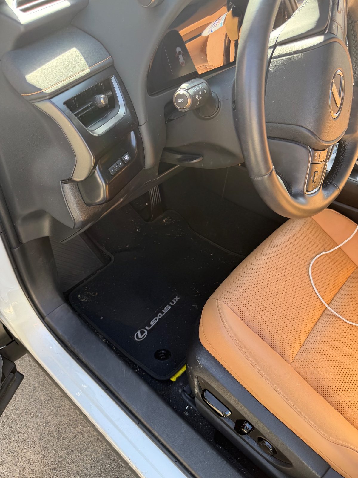 Driver footwell of a white Lexus UX before detailing with dust and debris on the mat