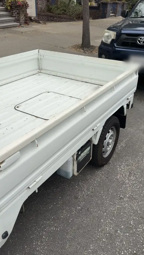 Dirty ribbed steel cargo bed of a Honda Acty kei truck before cleaning, grit and leaf debris scattered across the floor.