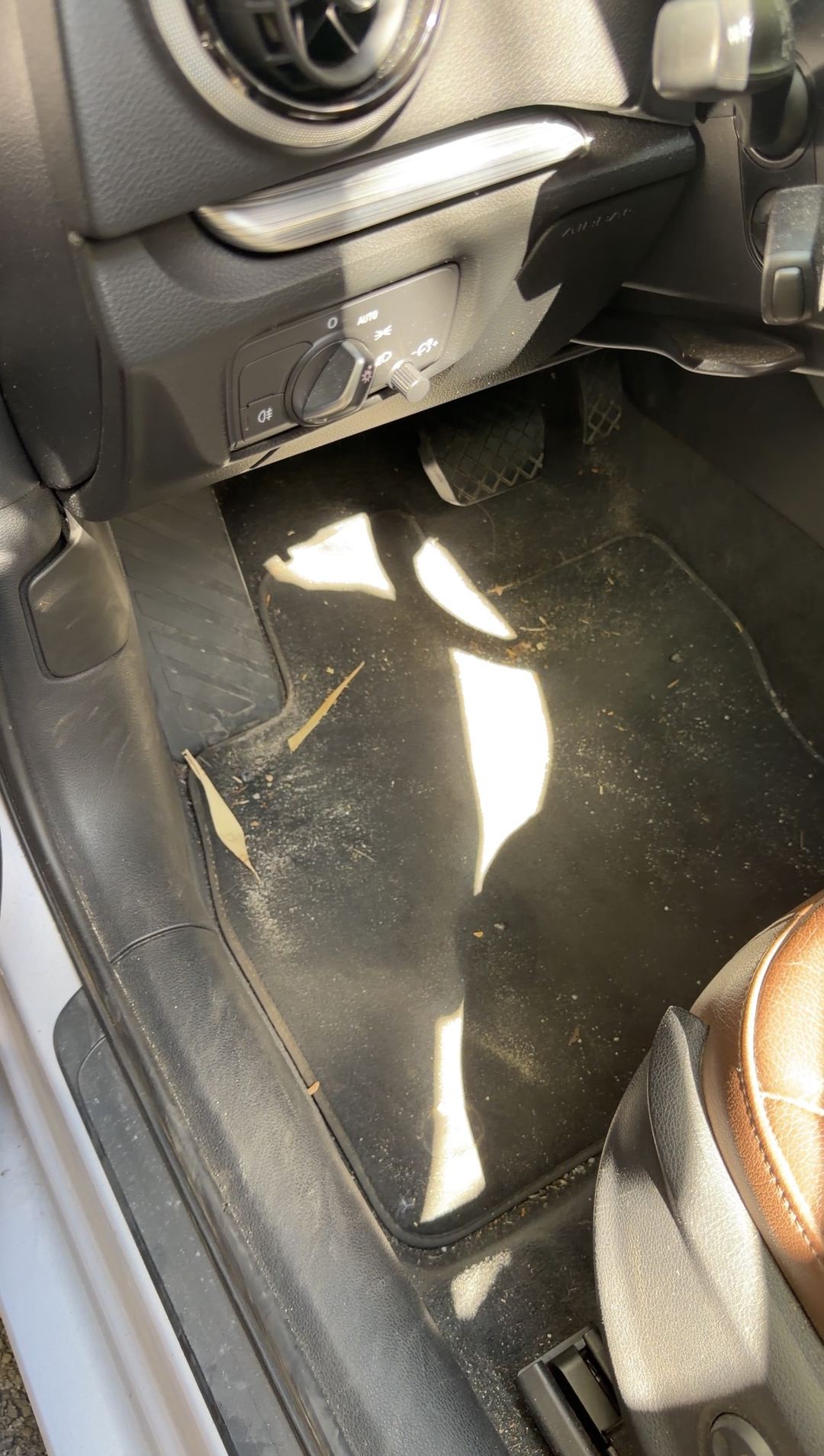 Driver footwell of a silver Audi A3 with grit and leaf fragments on the floor mat
