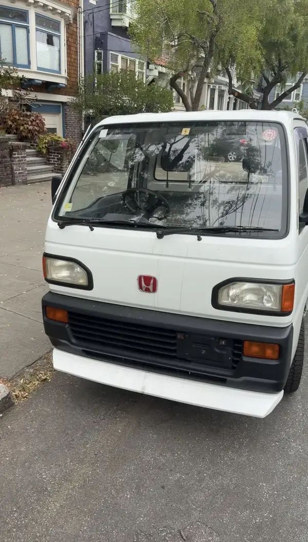 White Honda Acty kei truck photographed head-on at a San Francisco kerb before detailing, front panel dulled by road grime.