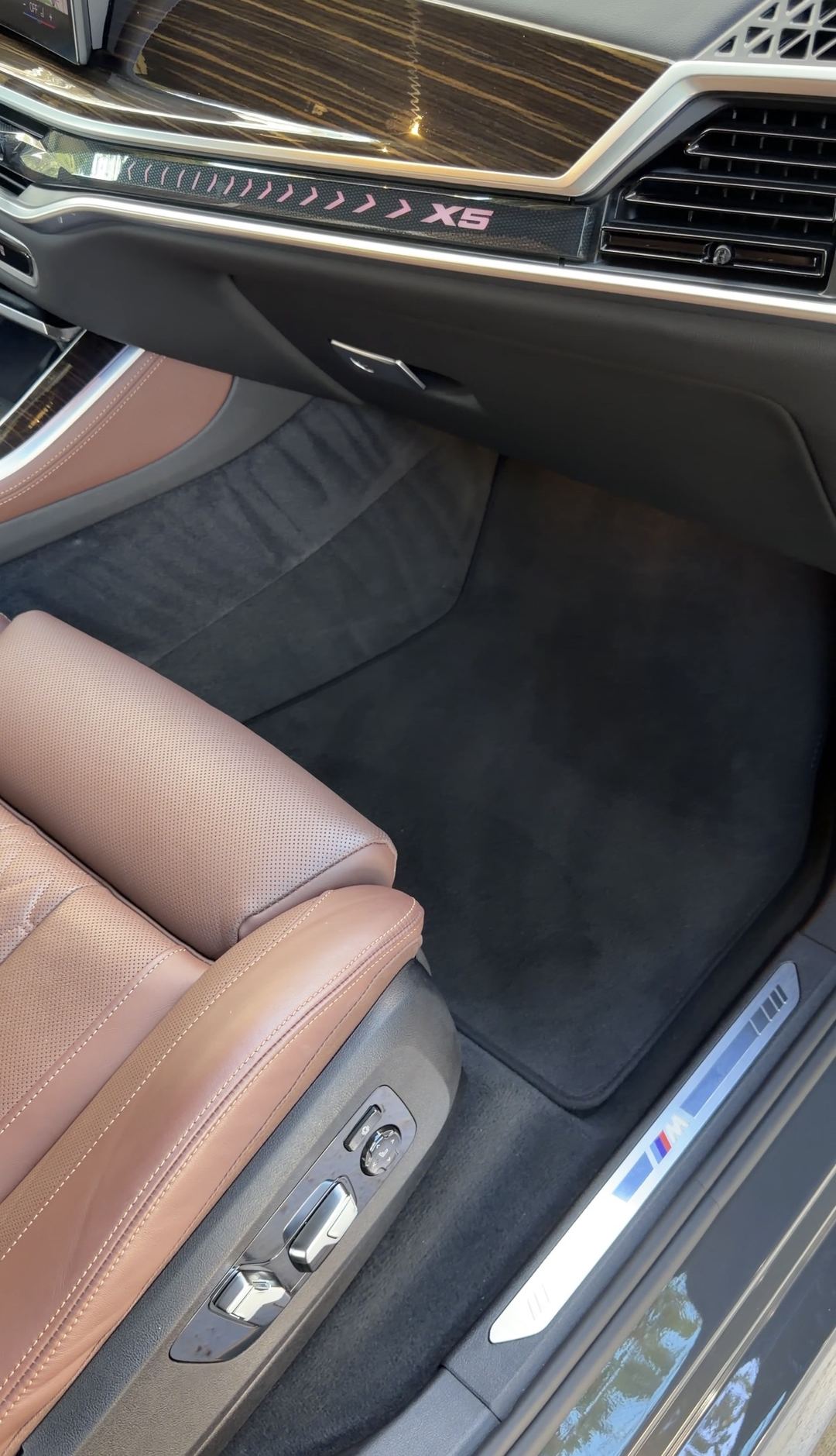Front passenger footwell of a BMW X5 after vacuuming, with the illuminated X5 dash trim above