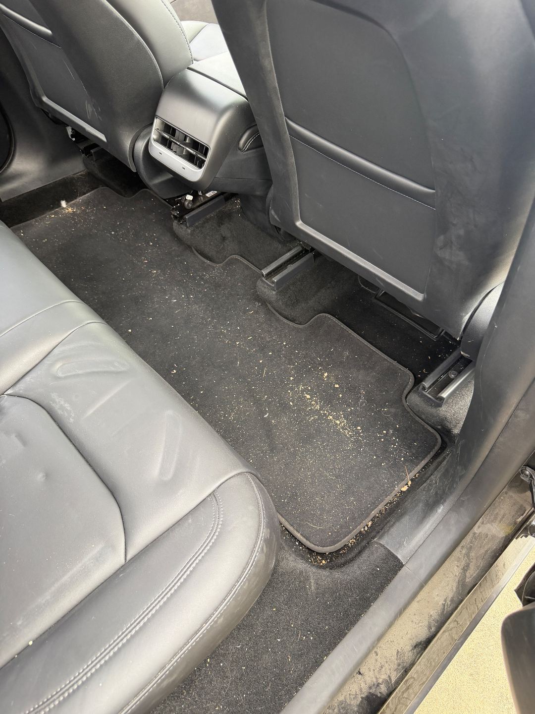 Rear footwell of a black Tesla Model Y before detailing, covered in sand and crumbs