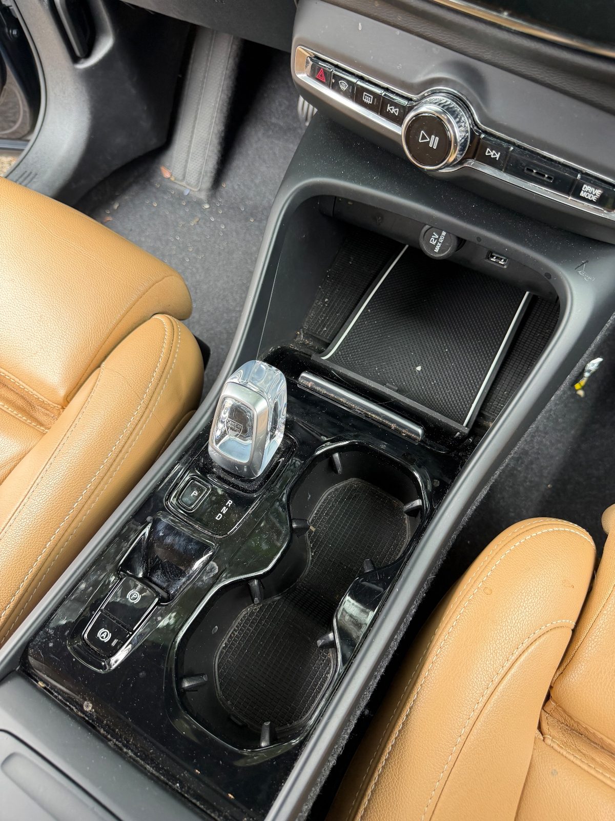 Centre console of a Volvo XC40 before detailing, with dust and crumbs in the charging tray and cupholders