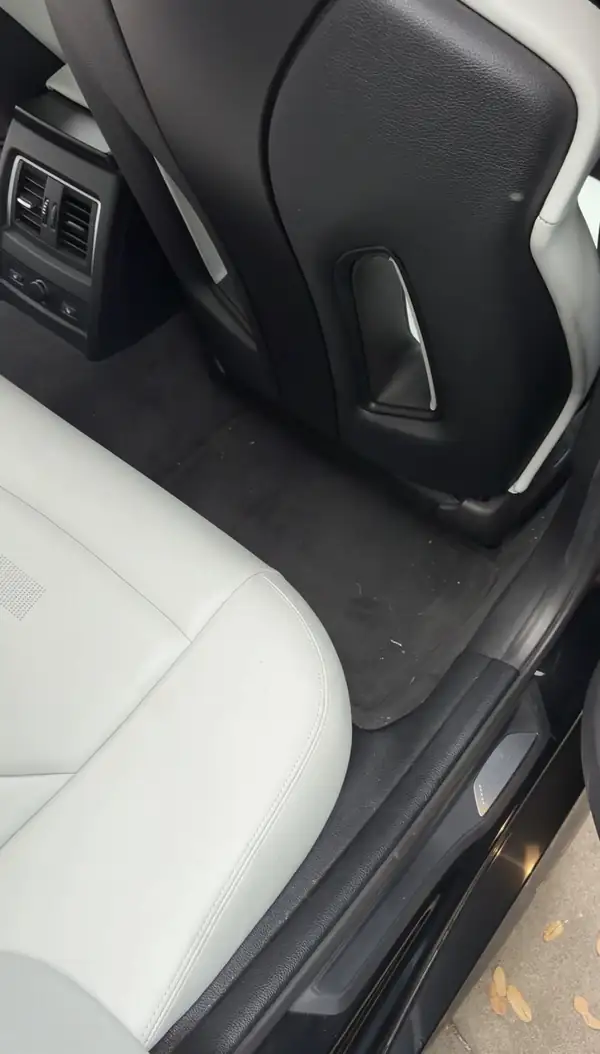 Left rear footwell of a BMW M3 before cleaning, with crumbs scattered across the black floor mat