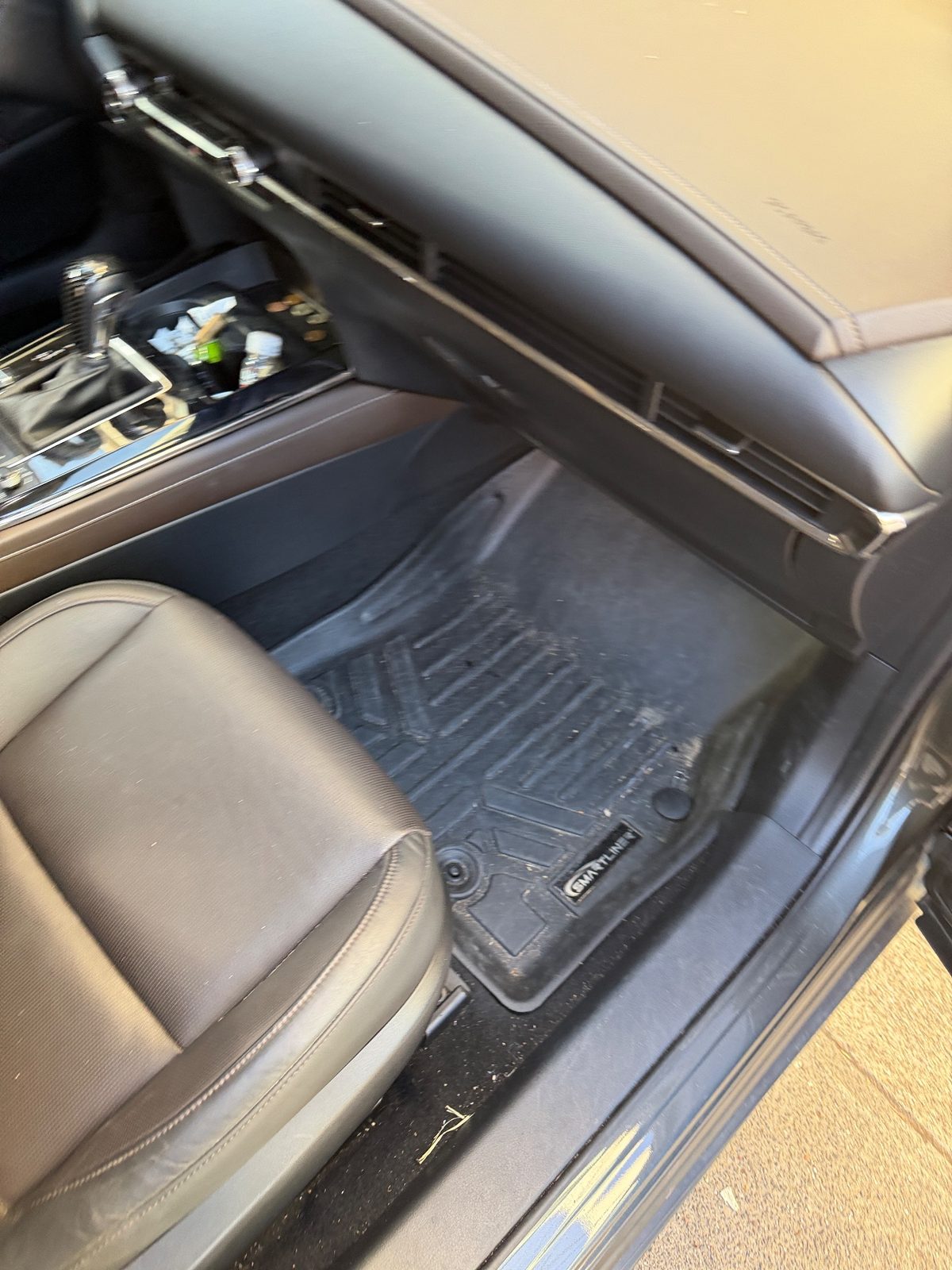 Front passenger footwell of a grey Mazda CX-30 before cleaning, liner covered in dirt