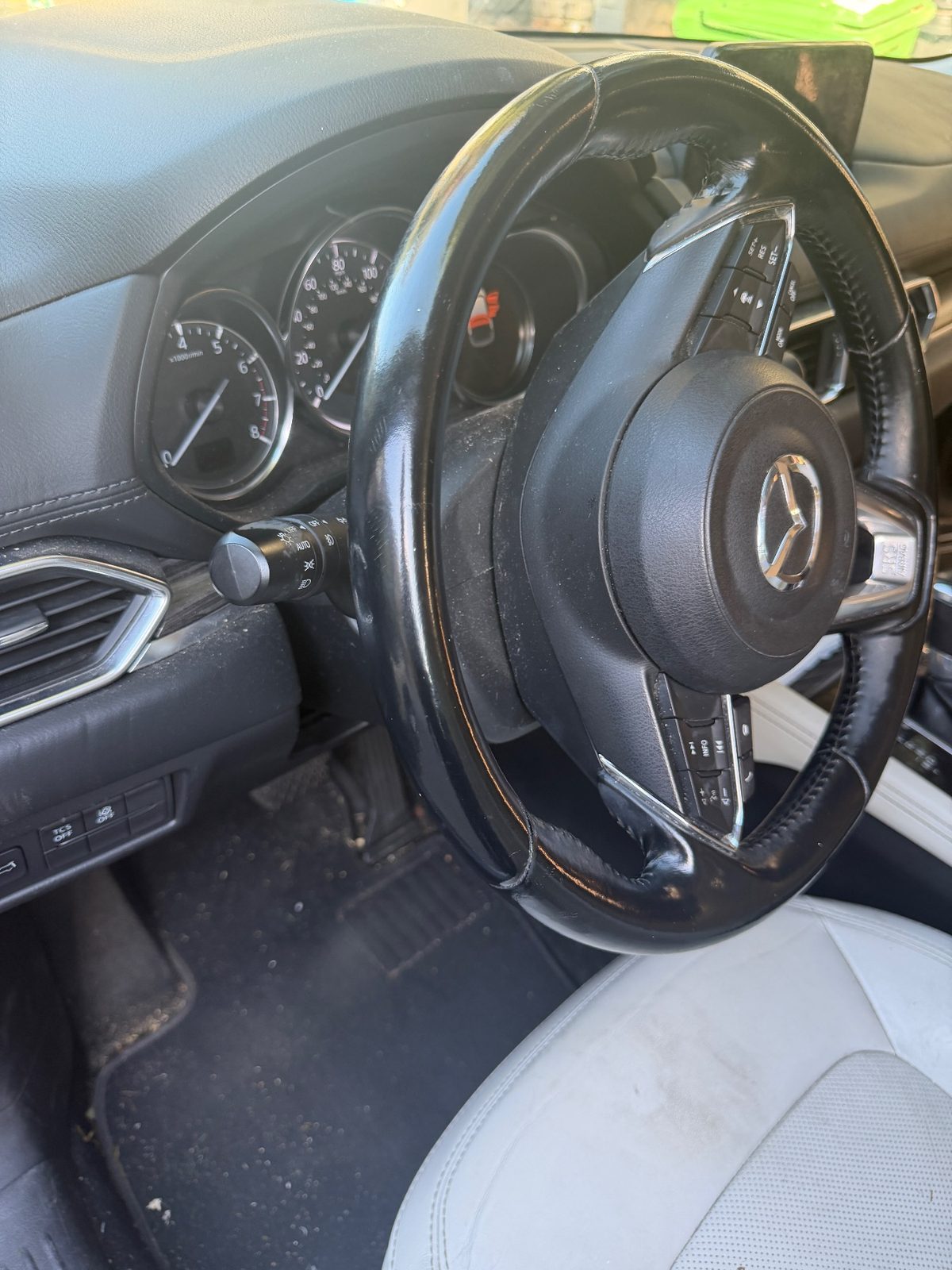 Steering wheel and dashboard of a dark blue Mazda CX-5 before detailing, dust on the vents and debris on the mat