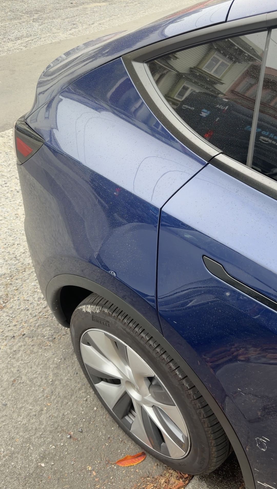 Rear quarter panel and wheel of a blue Tesla Model Y covered in dried water spots before washing.