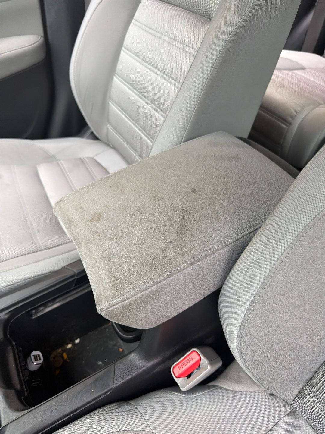 Grey cloth centre armrest of a maroon Honda CR-V before detailing, marked with dark drip stains