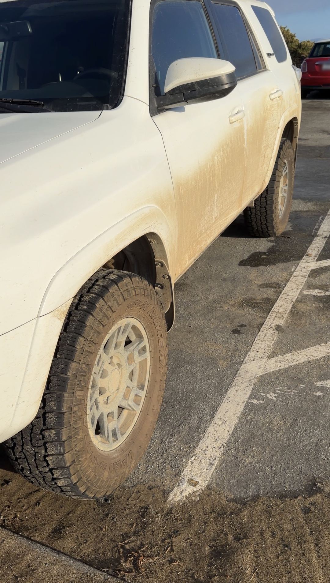 Driver side of a white Toyota 4Runner with tan mud spray on the doors and dust-caked wheels
