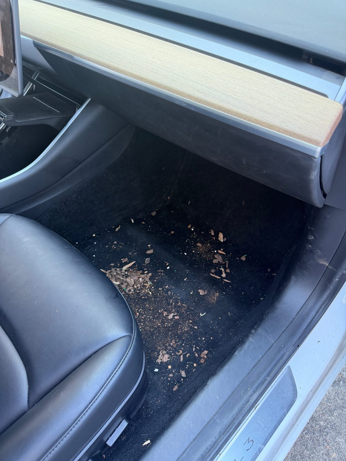 Passenger footwell of a white Tesla Model 3 before detailing, covered in debris and crumbs
