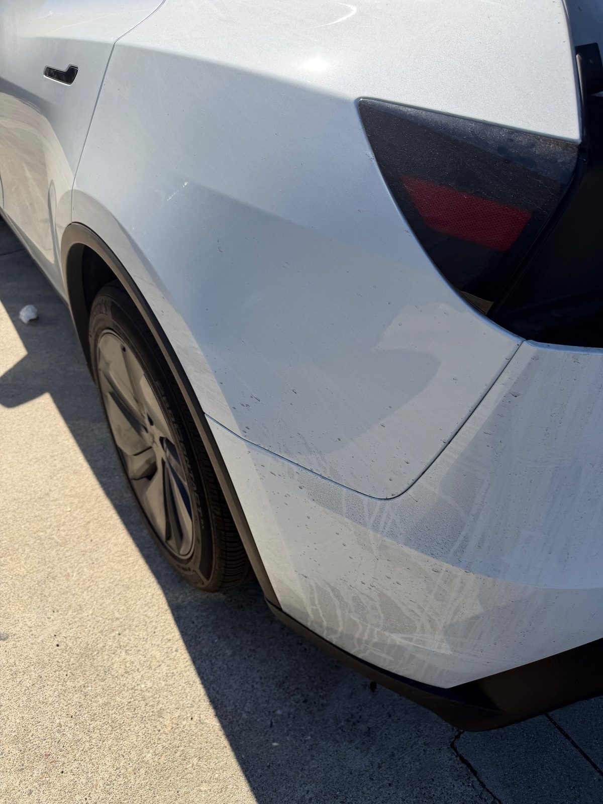 Rear quarter and bumper of a white Tesla Model Y before washing, dust and white drip streaks