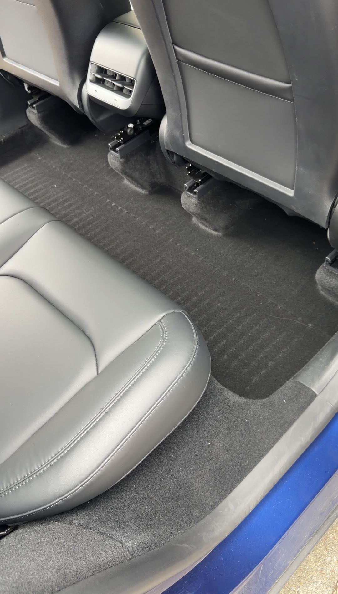 Rear passenger-side footwell of a Tesla Model Y with the floor liner removed before cleaning.