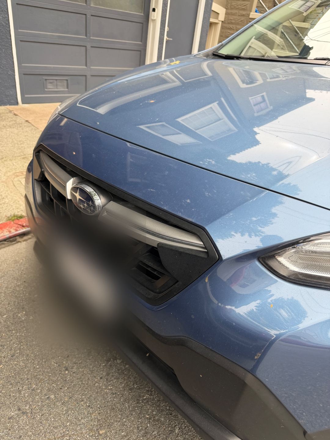 Front grille and hood of a blue Subaru Crosstrek before washing, with dust and debris specks on the paint