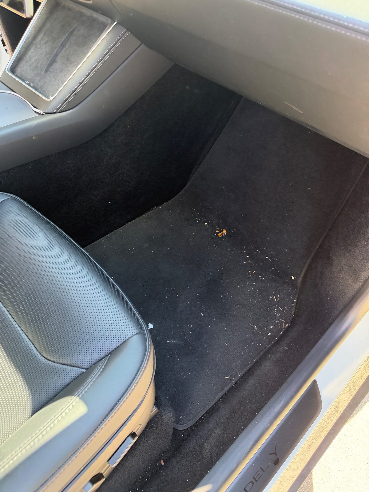 Front passenger footwell of a white Tesla Model Y before detailing, crumbs and grit on the black mat
