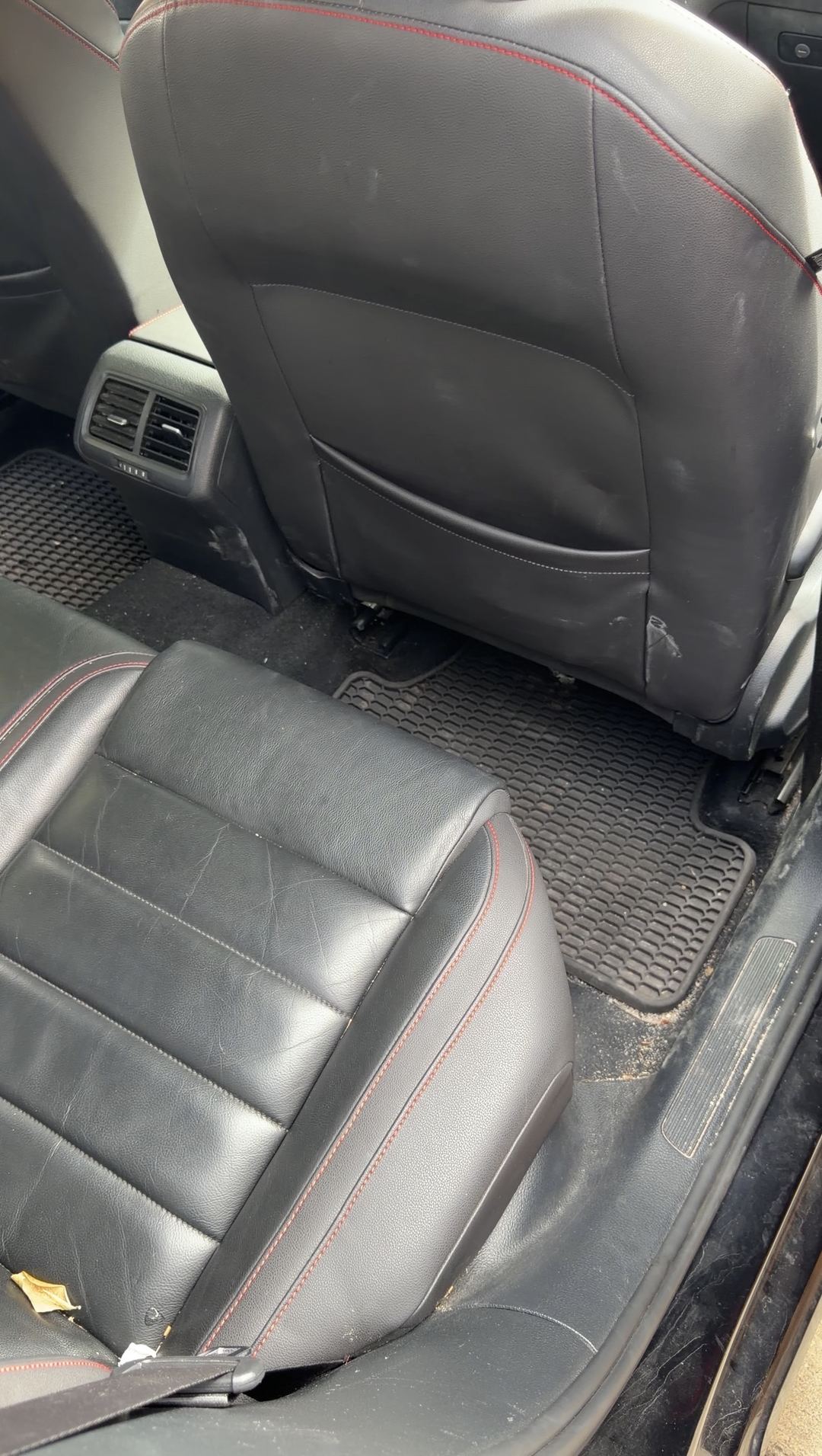 Rear passenger-side footwell of a black VW GTI before cleaning, debris on the mat