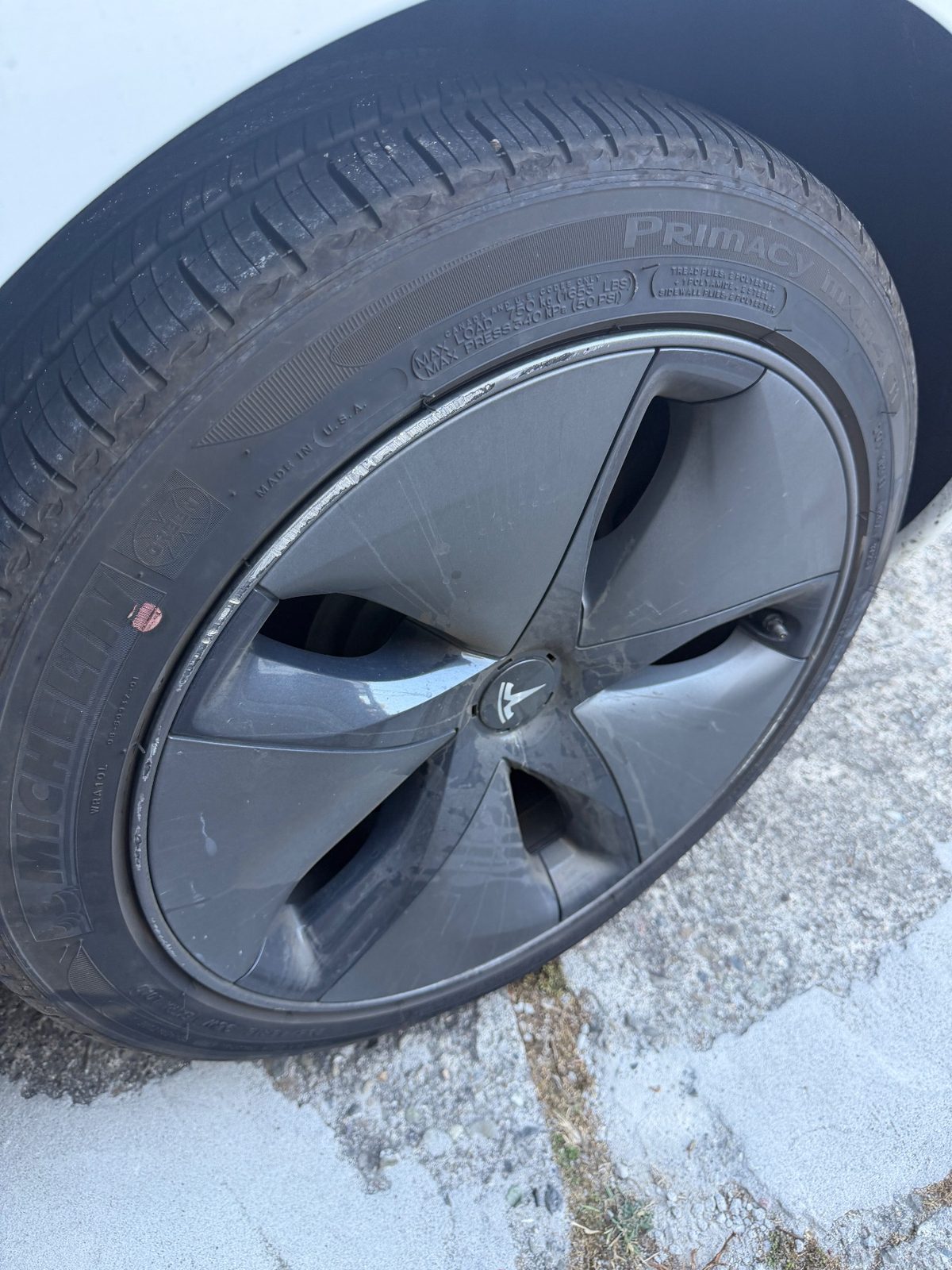 Dirty aero wheel cover and tyre on a white Tesla Model 3 before detailing