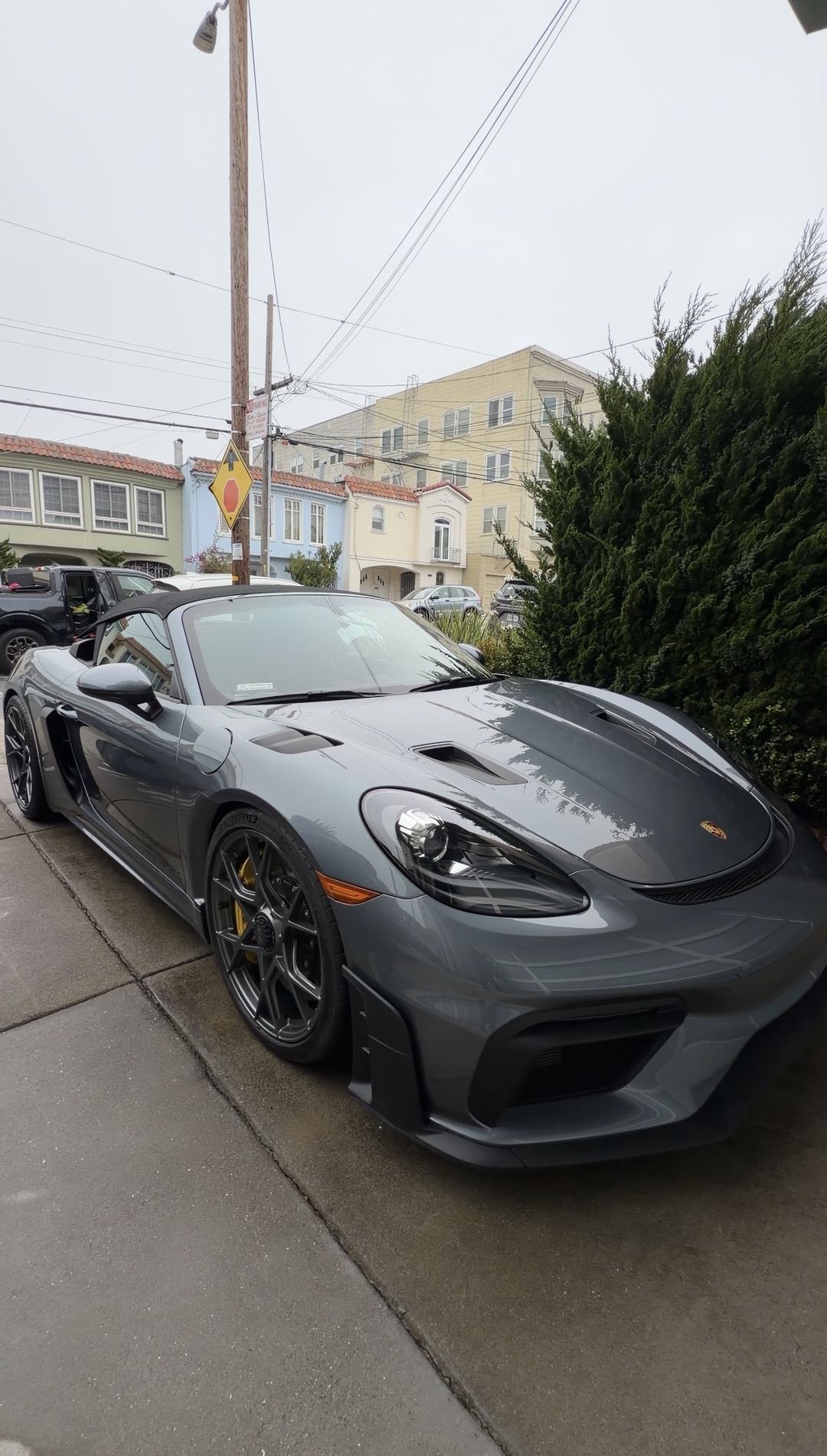 Clean grey Porsche 718 Spyder RS with its black soft top up, parked on a San Francisco driveway after a mobile detail.