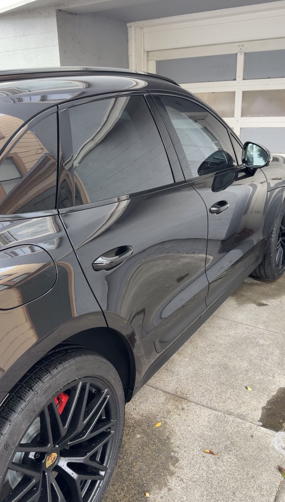 Clean driver's side of a black Porsche Macan GTS after a mobile exterior detail, water still beading on the wheel.