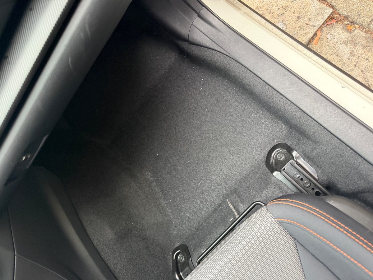 Bare front passenger footwell carpet of a Subaru Crosstrek with the mat removed before cleaning