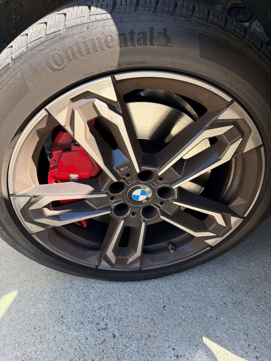 Front wheel of a grey BMW X1 with red brake caliper before detailing