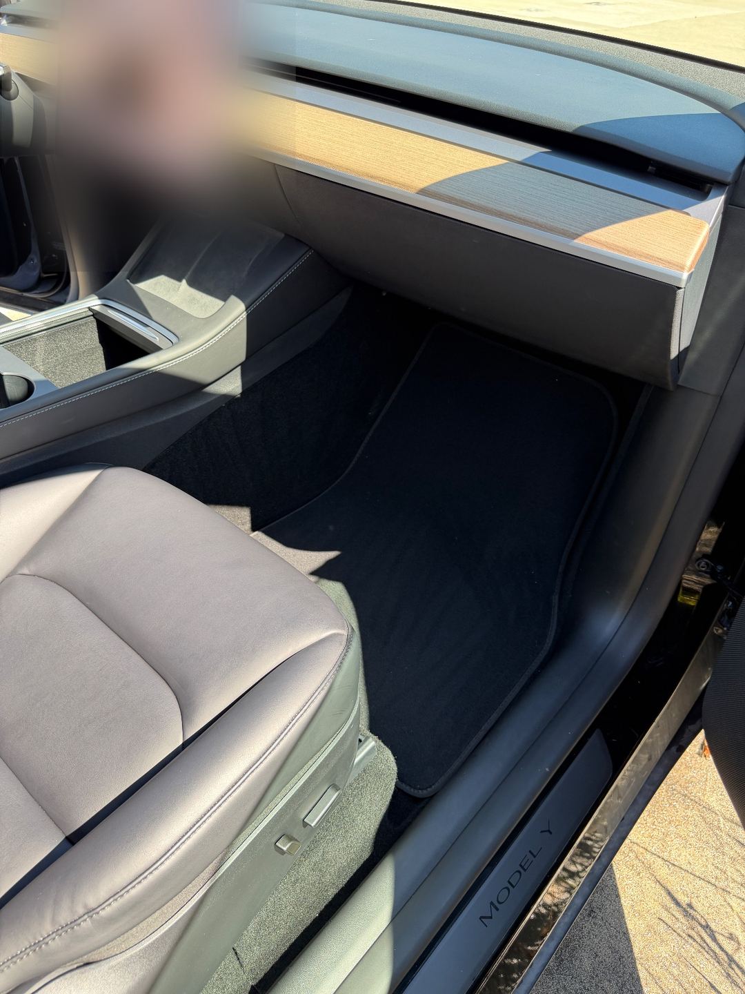Front passenger footwell of a black Tesla Model Y after detailing, the floor mat clean
