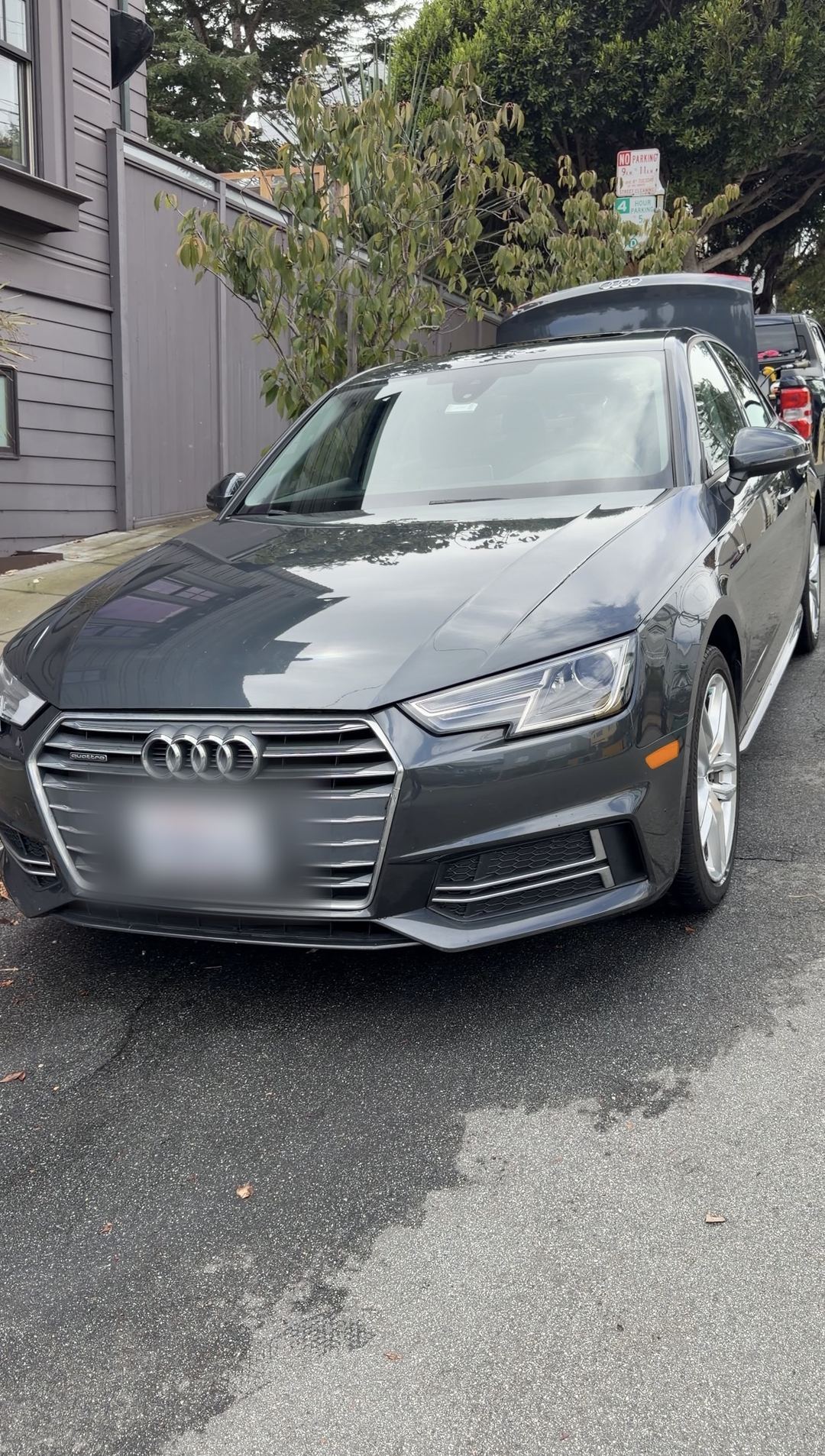 Freshly washed grey Audi A4 sedan, front three-quarter view on a wet residential street