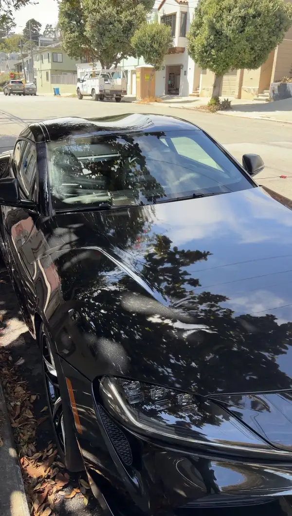 Gloss black Toyota GR Supra hood and windshield after a wash, reflecting a tree canopy on a San Francisco residential street.
