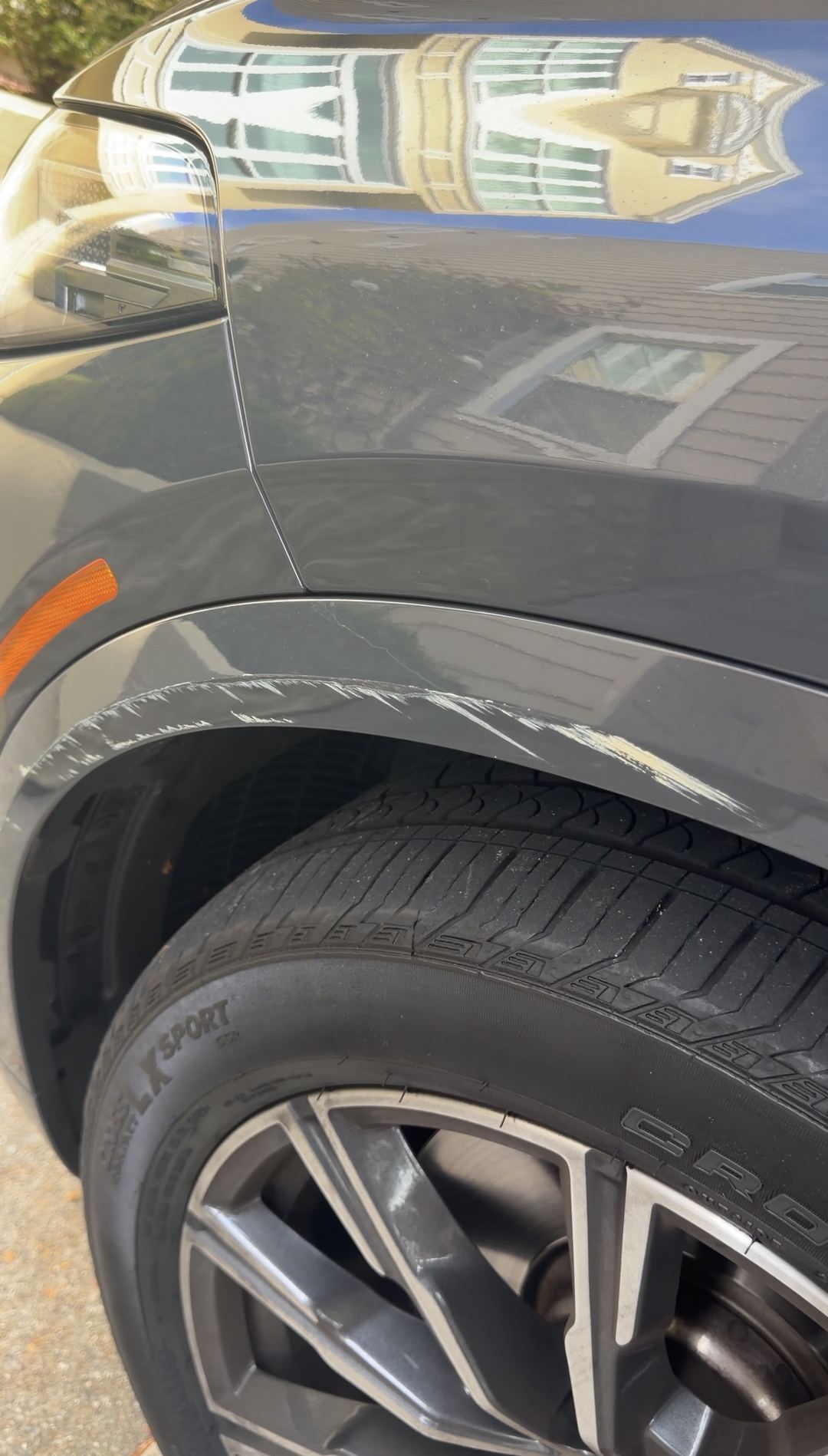 Front right wheel arch of a dark grey BMW X5 before correction, with a long white scuff scraped along the arch lip
