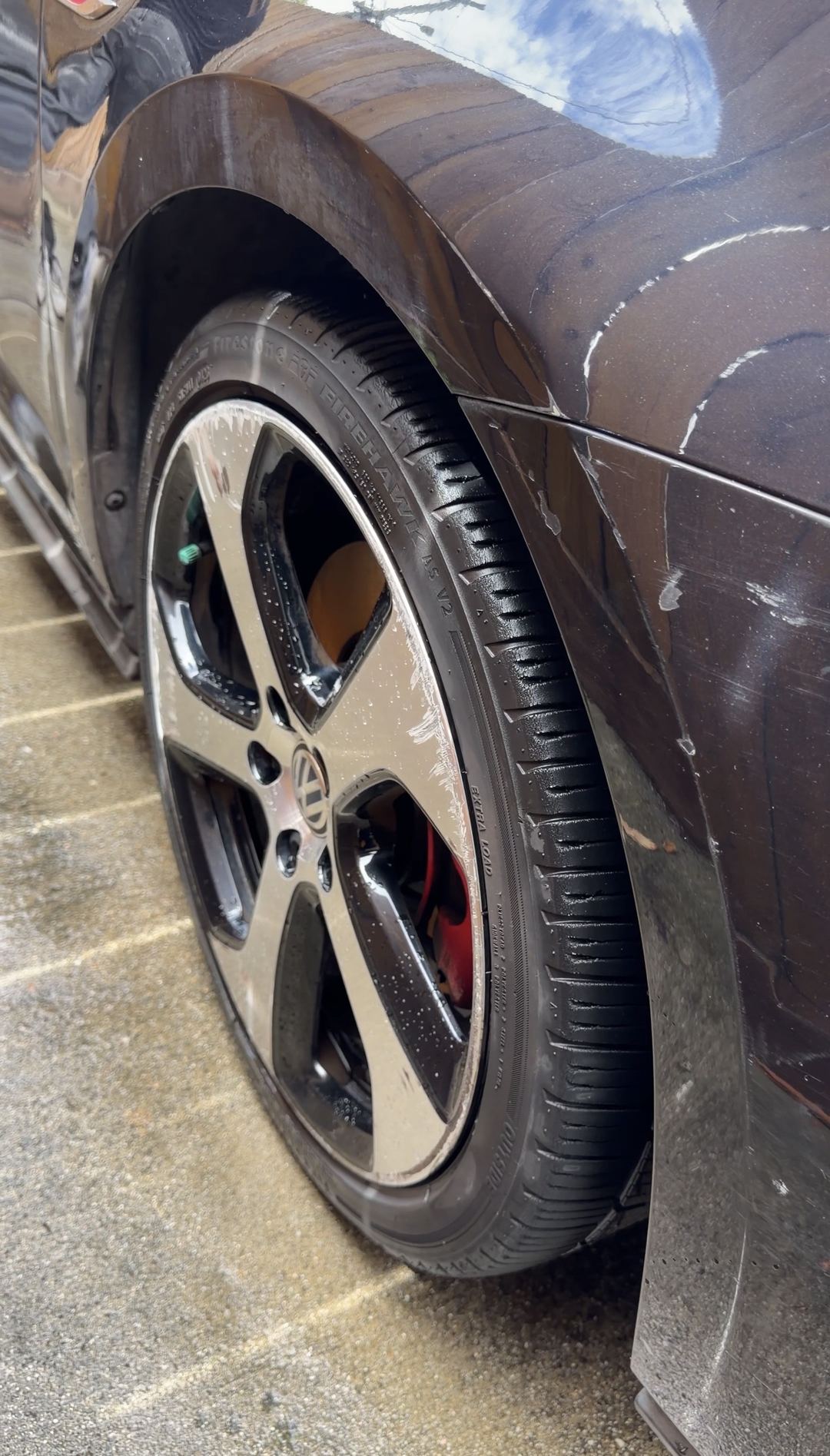 Front wheel of a black VW GTI after washing, whitish marks visible on the paint beside it