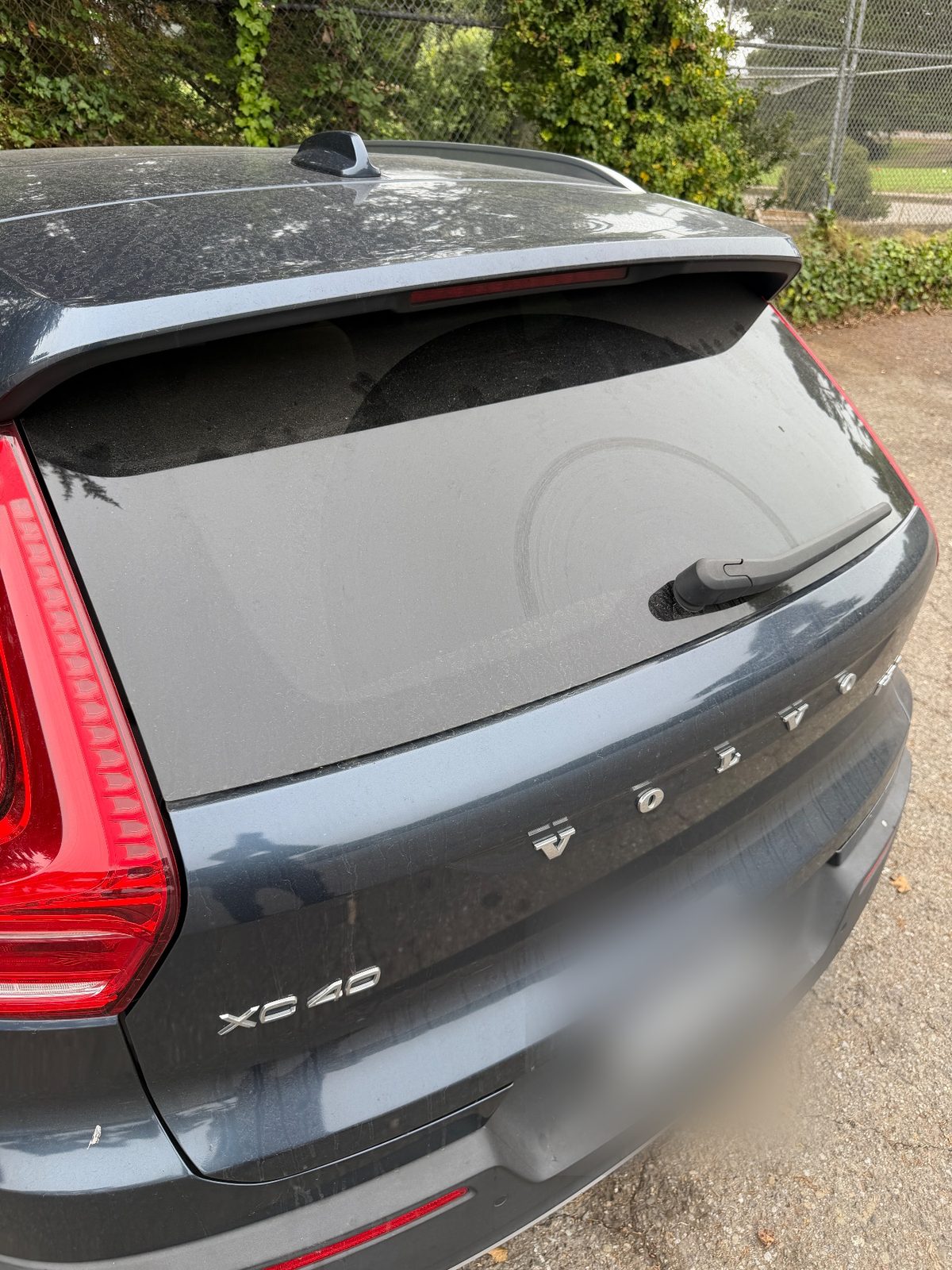 Rear of a Volvo XC40 before washing, with a thick dust film on the tailgate glass
