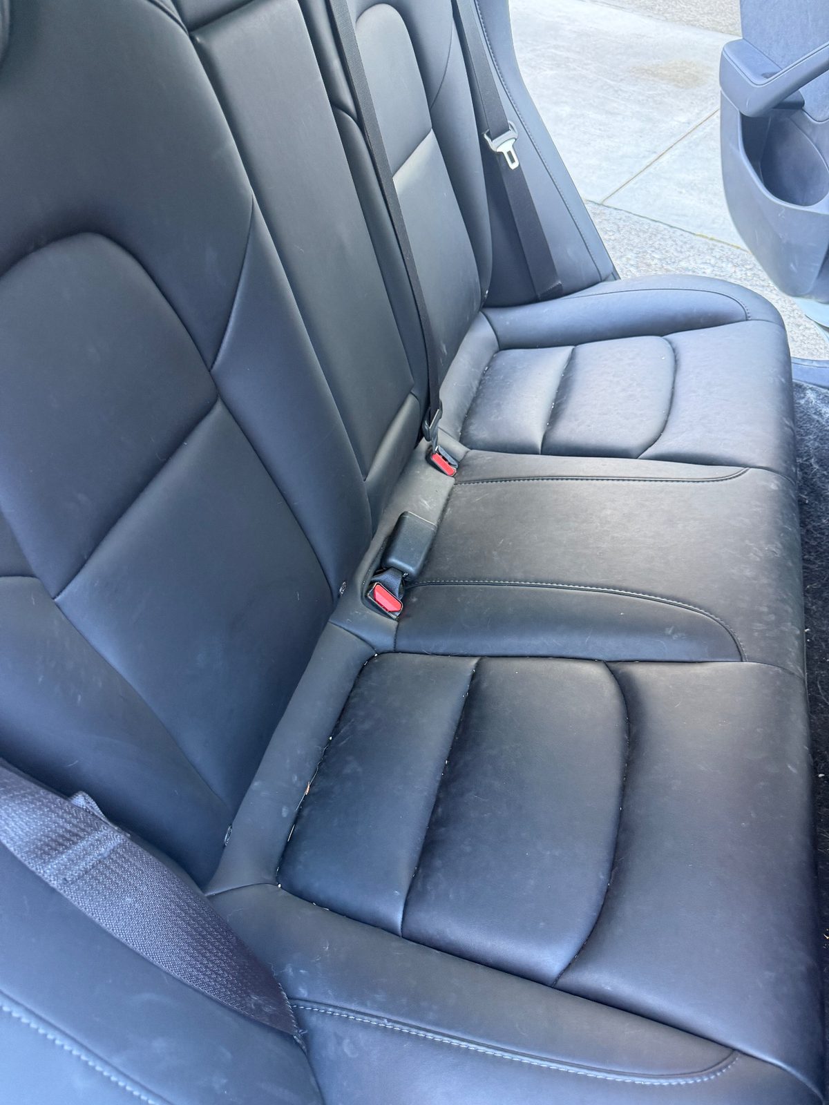 Rear bench seat of a white Tesla Model 3 before detailing, dusty leather with debris in the seams